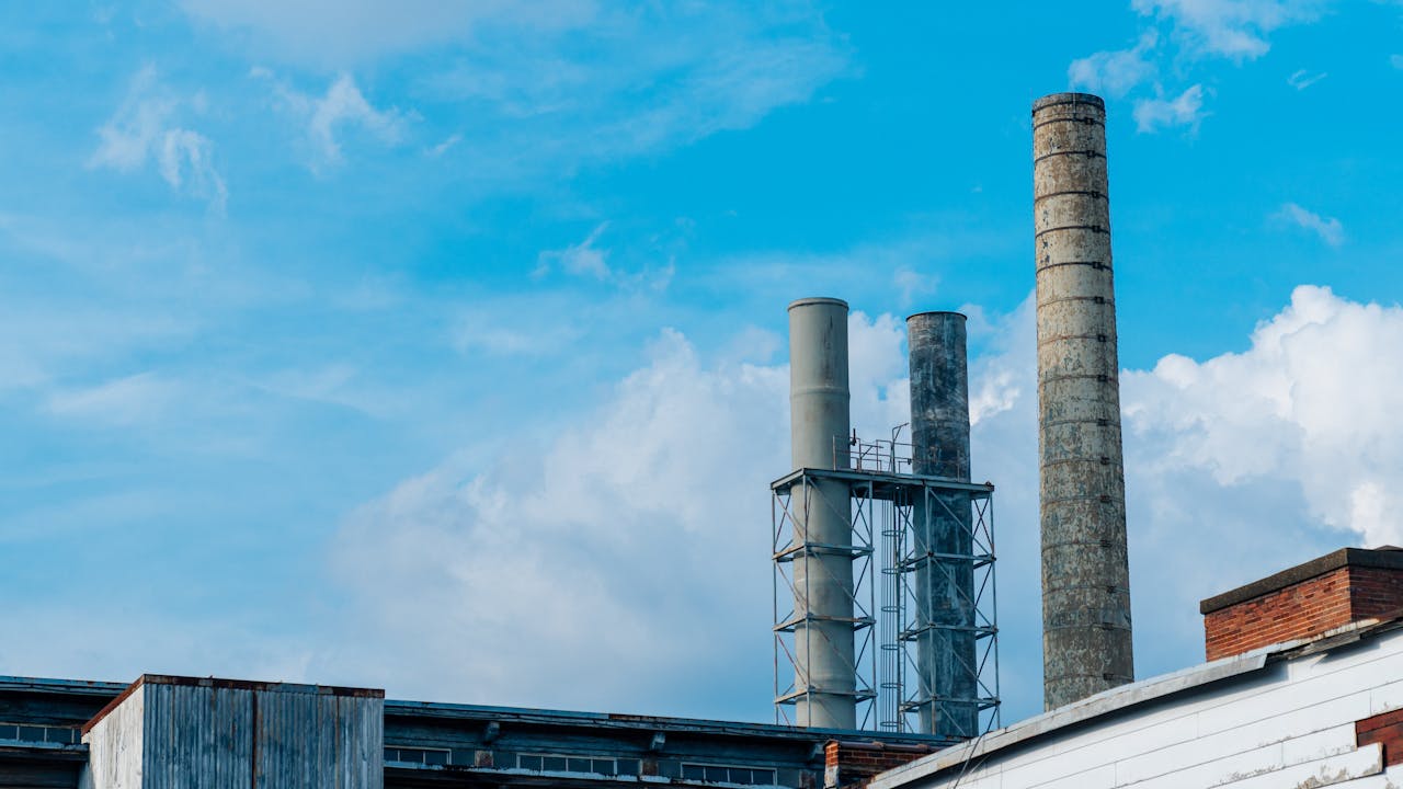 A view of industrial factory chimneys with a bright blue sky and clouds in the background.